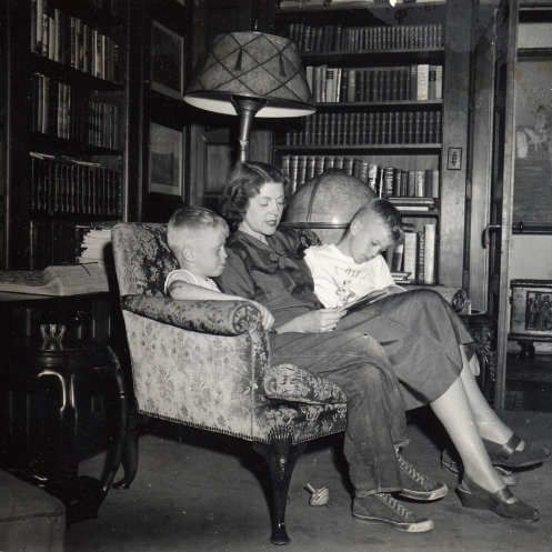 A vintage photo of Mary Koch reading to Charles Koch and David Koch, seated on a sofa in the family den.